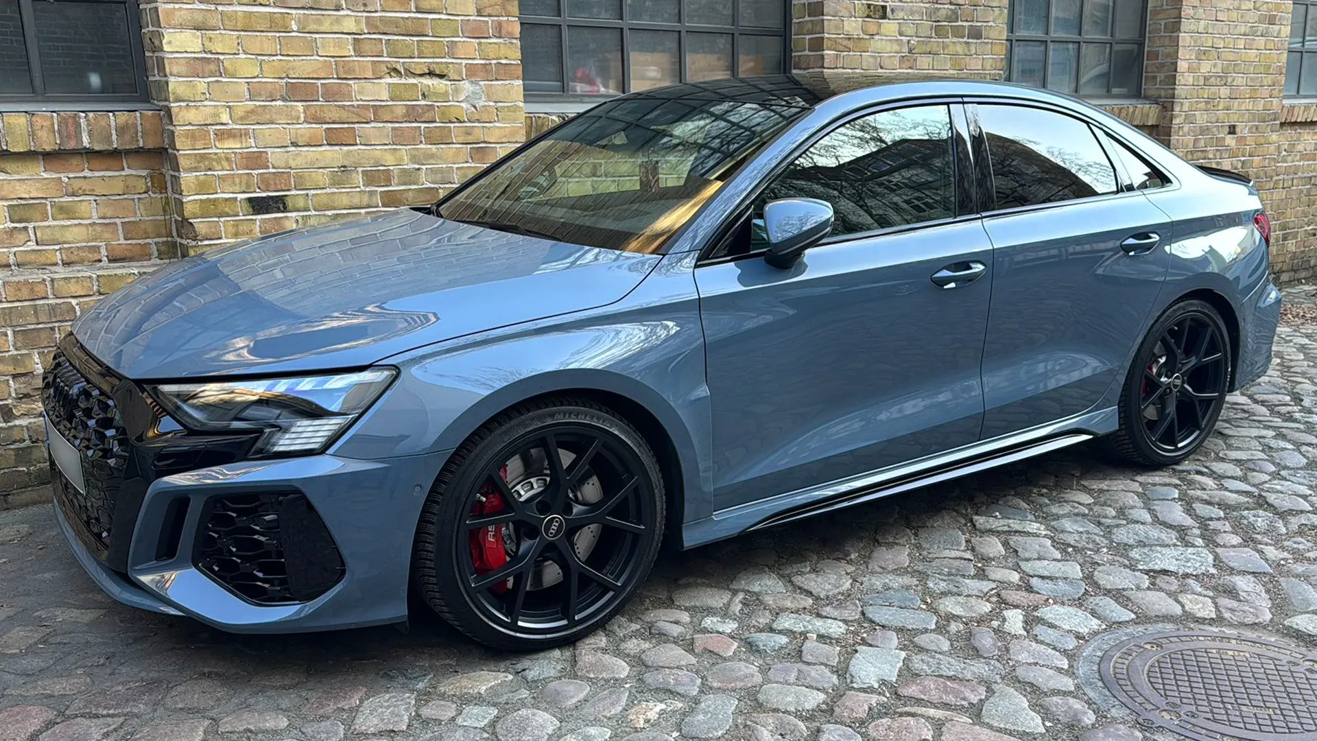 Hellblauer Audi RS 3 auf Kopfsteinpflaster vor der Werkstatt