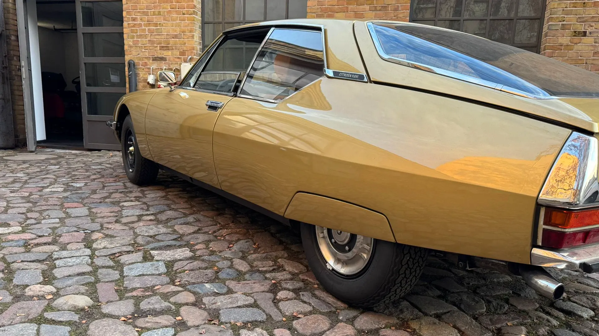 Goldfarbener Citroën SM auf Kopfsteinpflaster vor der Werkstatt